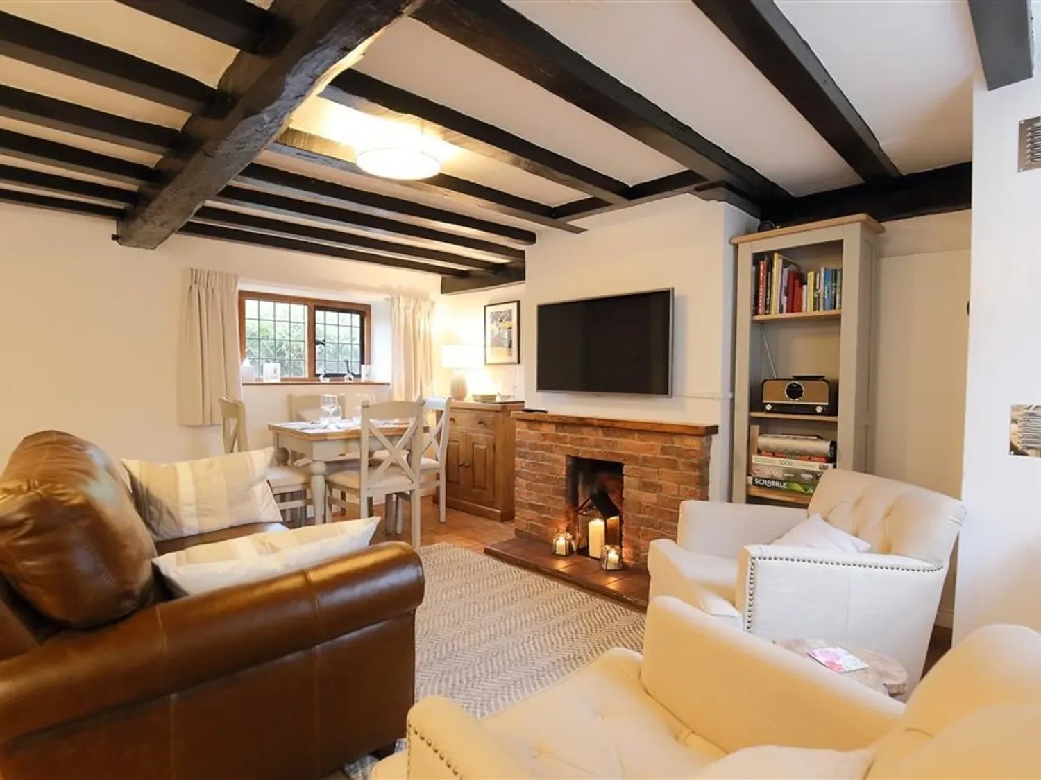 A living room with a brown leather sofa white armchairs dining table and brick fireplace at One Masons Court in Stratford upon Avon