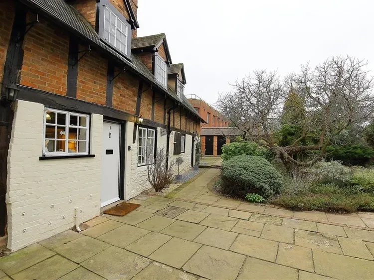 A paved courtyard beside a brick-and-white building, with shrubs and leafless trees.