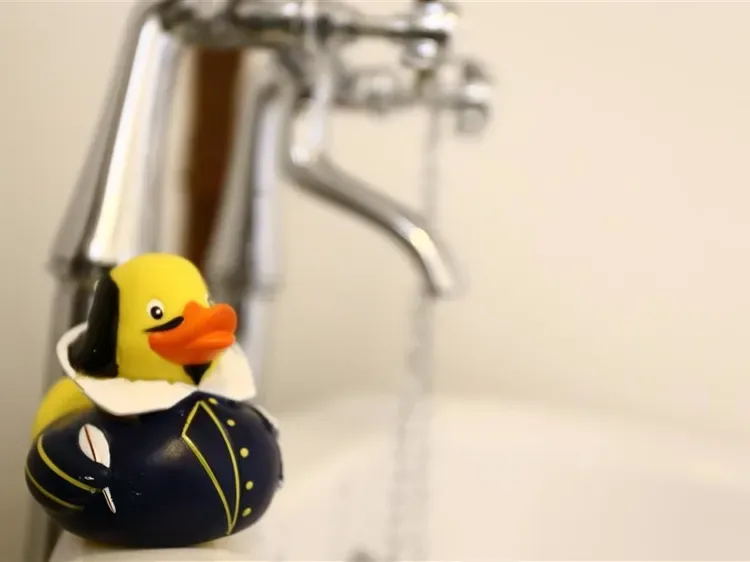 A yellow rubber duck sits beside a faucet in a bathroom sink area.