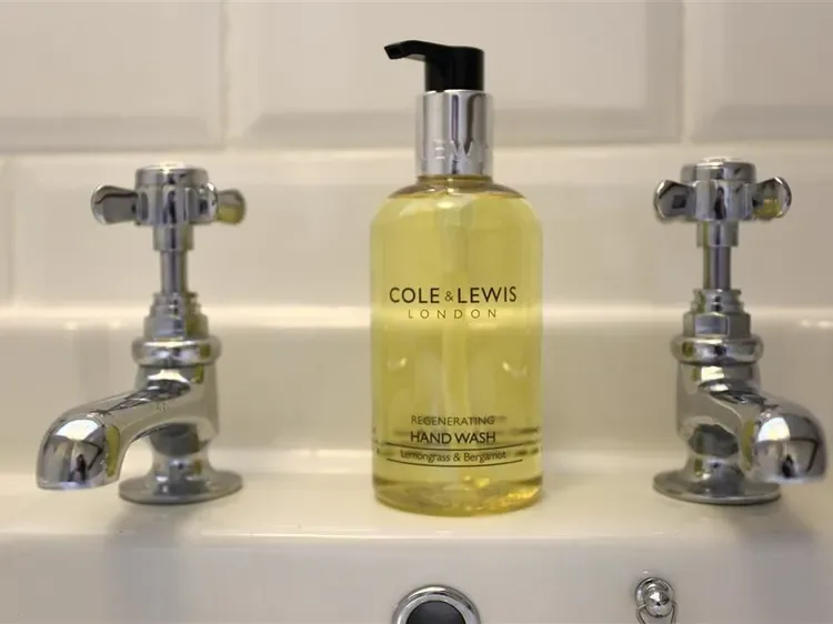 A bathroom sink with a yellow hand-wash bottle between two chrome taps.