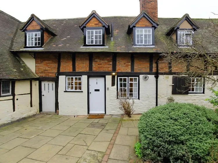 A traditional two-story house with dark timber framing, brickwork, and a paved front yard.