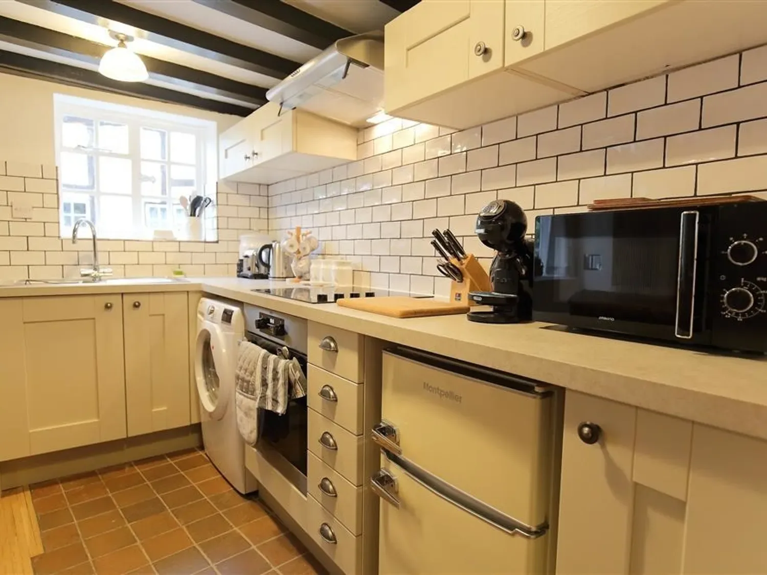 A kitchen with cream cabinets white tiled backsplash microwave coffee maker and a washing machine at One Masons Court in Stratford upon Avon
