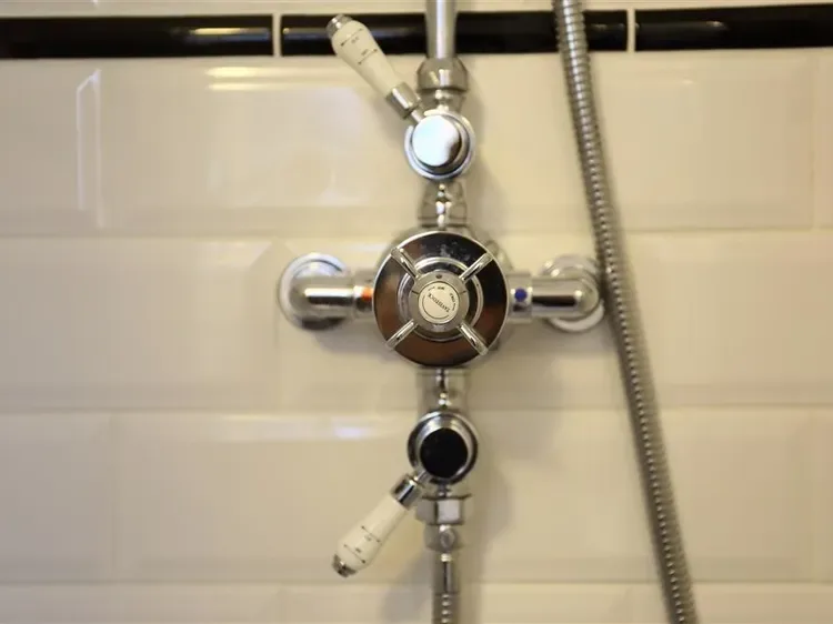 A shower fixture with chrome controls and a flexible hose against tiled walls.