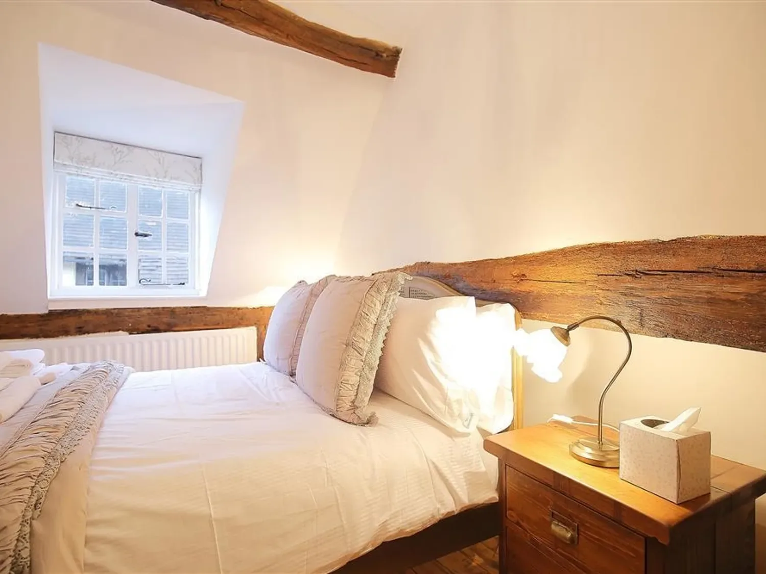 A bedroom with a bed beside a wooden nightstand and a lamp.
