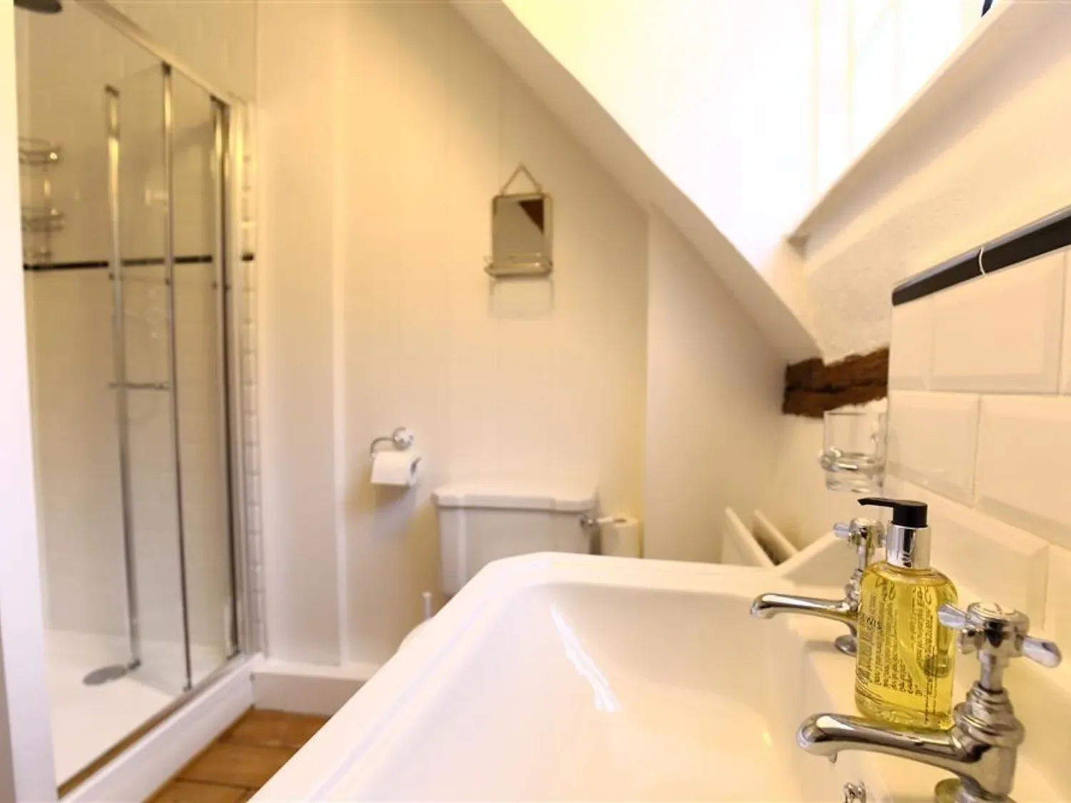 A bathroom with a glass shower, toilet, and sink with a soap dispenser.