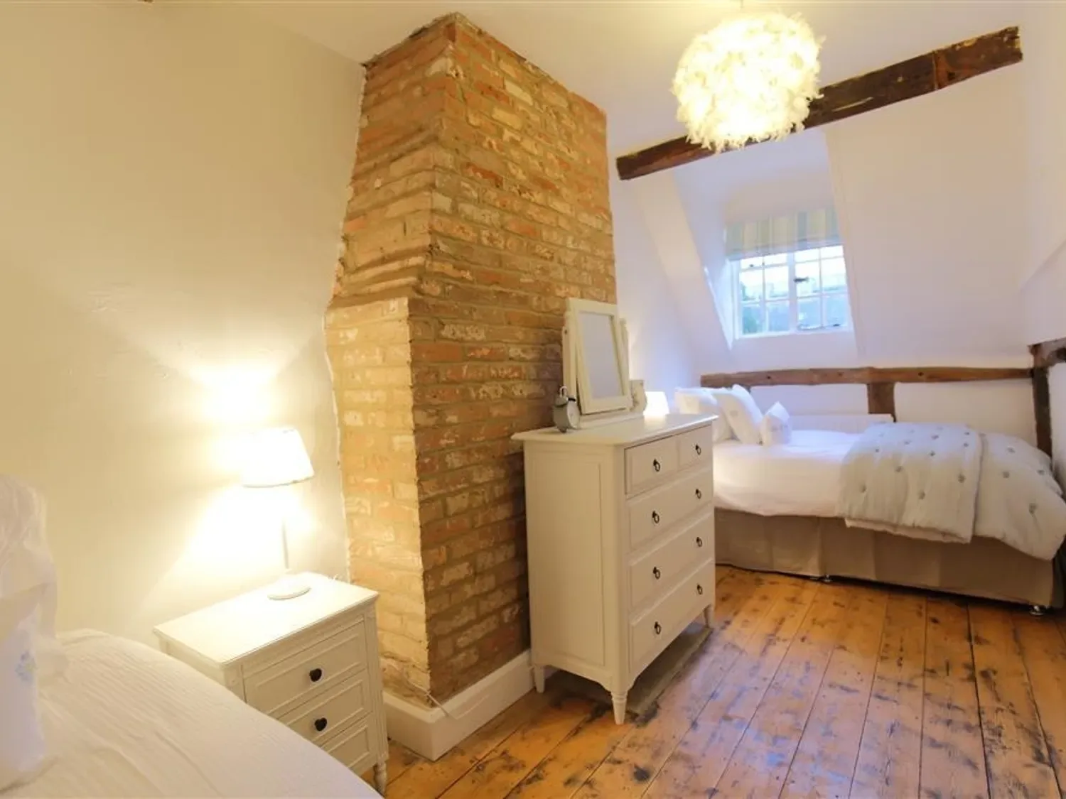 A bedroom with wooden flooring, white dressers, beds, and an exposed brick chimney.