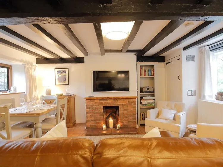 A living room with exposed ceiling beams, a brick fireplace, and seating.