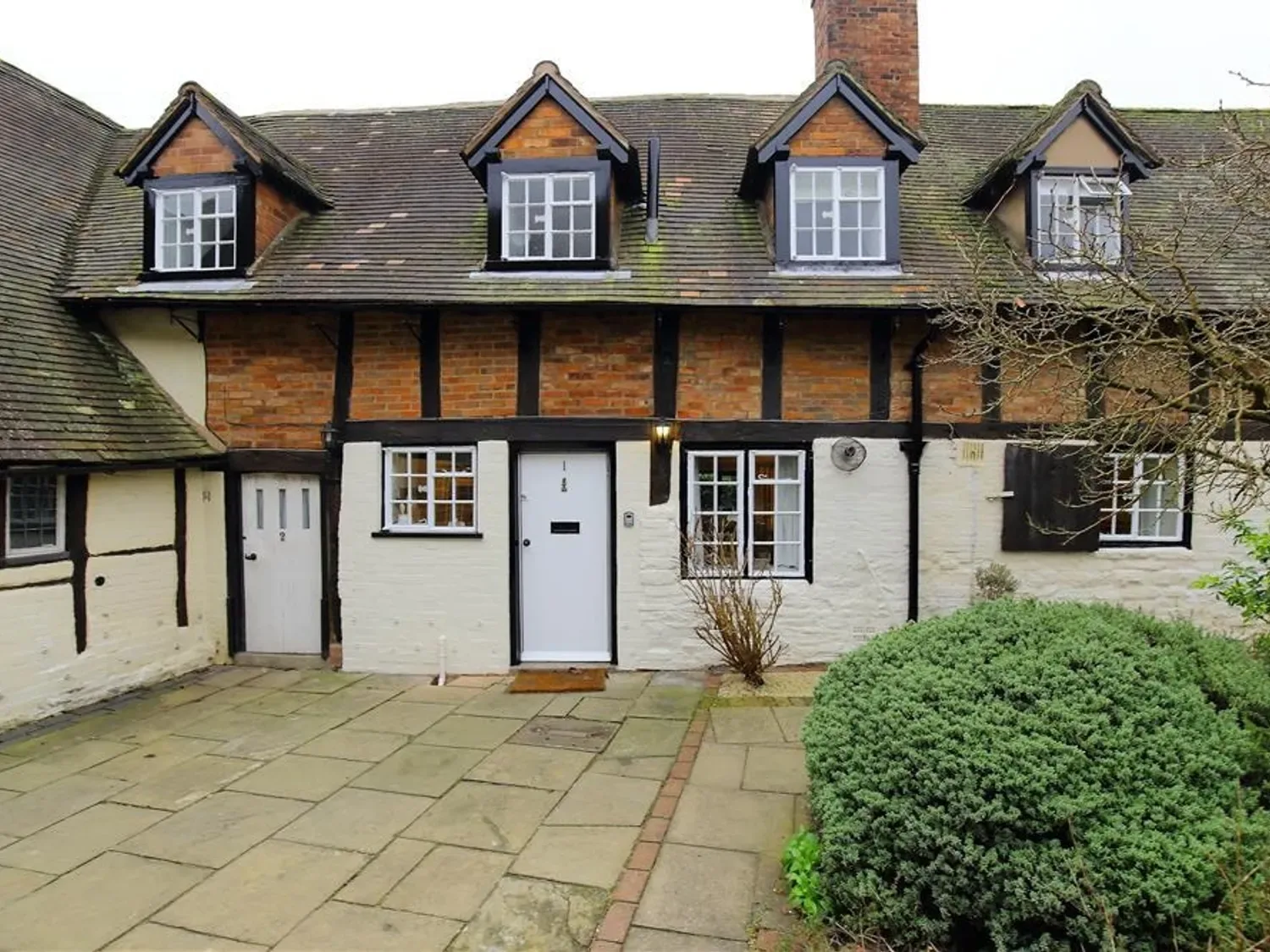 An exterior view of a brick and timber cottage with a tiled roof and paved courtyard at One Masons Court in Stratford upon Avon