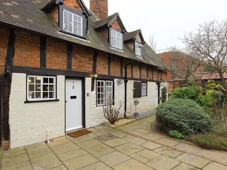 A cottage exterior with a paved walkway and shrubs.