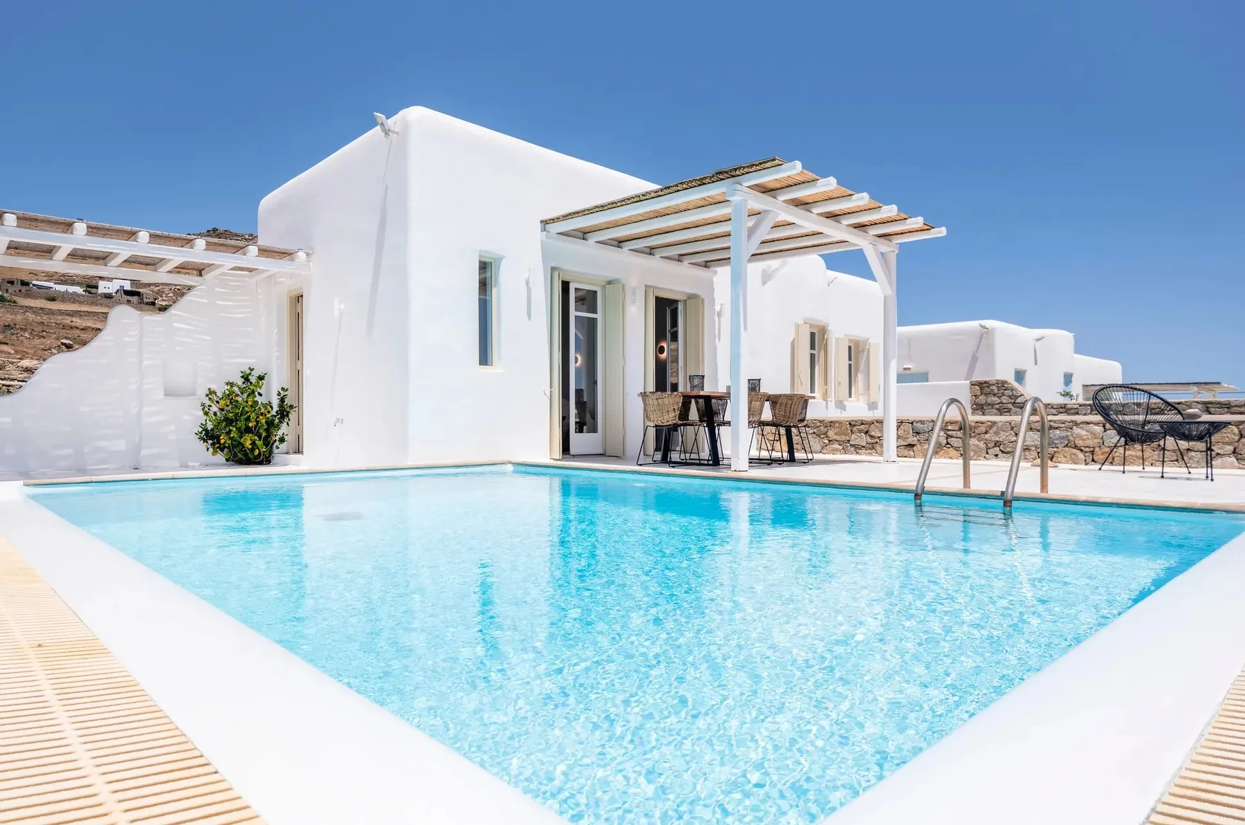 A bright outdoor pool beside a white building and shaded patio seating.