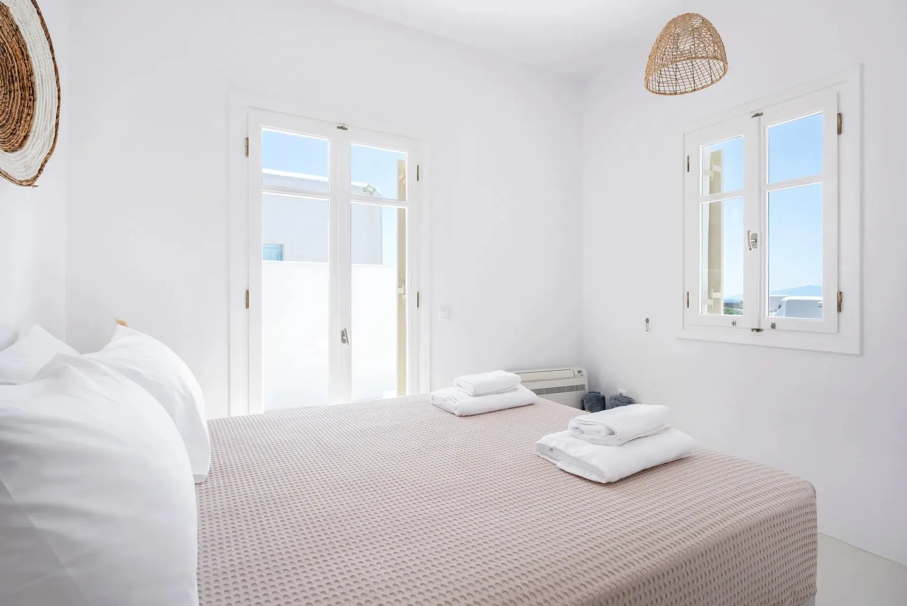A bright bedroom with a neatly made bed and windows overlooking the sea.
