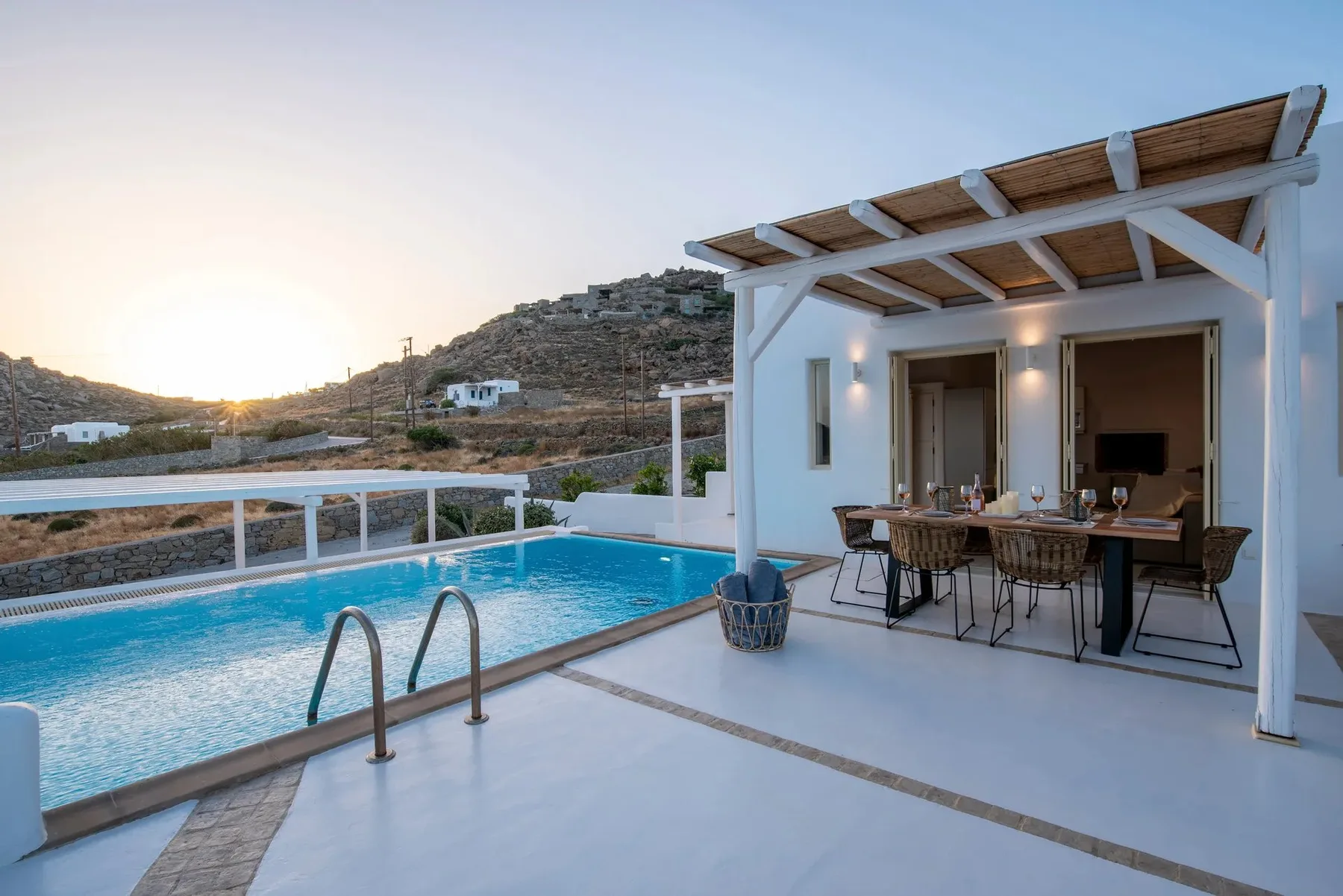 Una zona de comedor junto a la piscina, con una mesa exterior al atardecer.