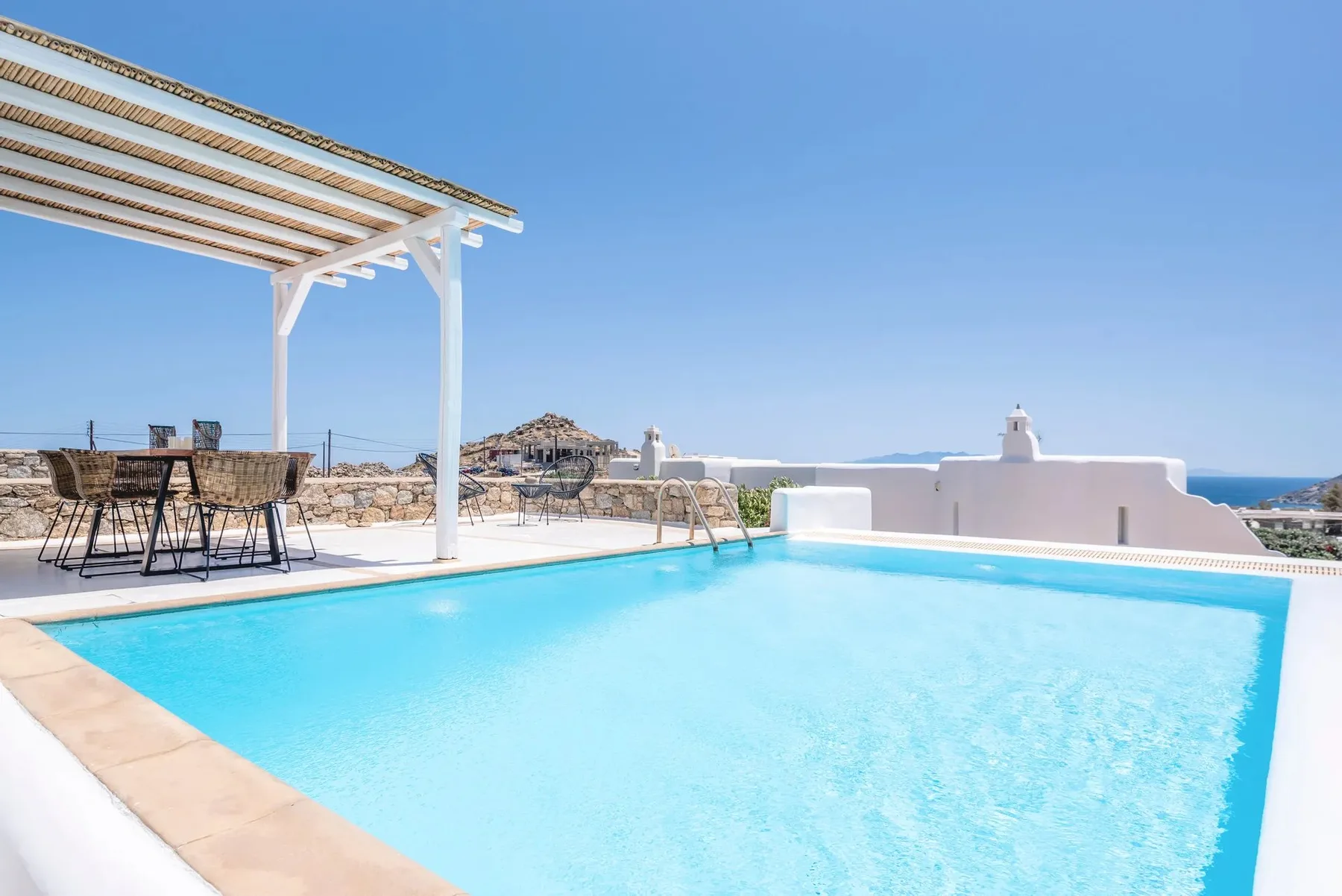 A bright outdoor swimming pool beside a shaded dining area and the sea.