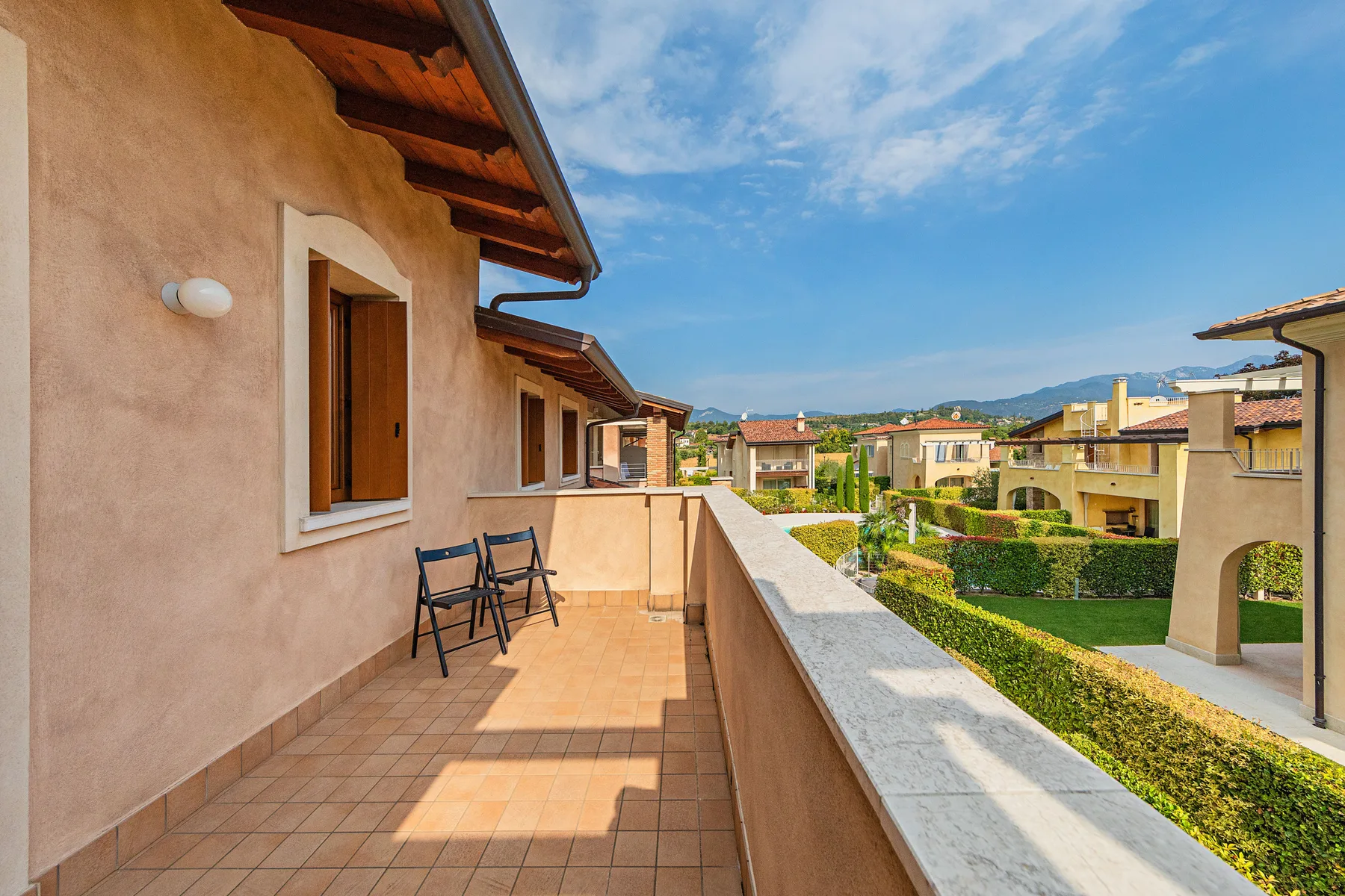 A tiled outdoor balcony overlooks landscaped grounds and nearby buildings.