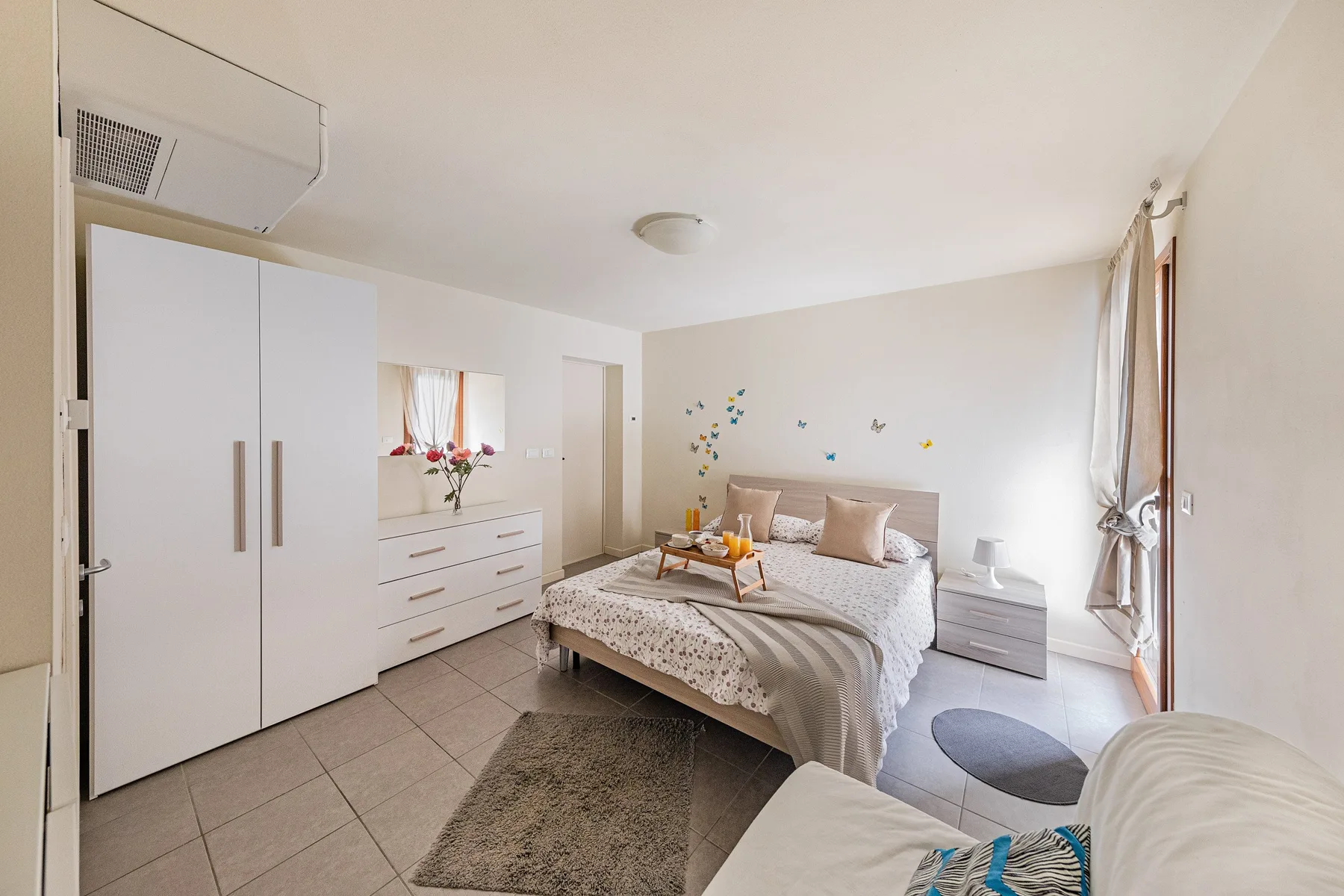 A bright bedroom with a double bed, wardrobe, and dresser.