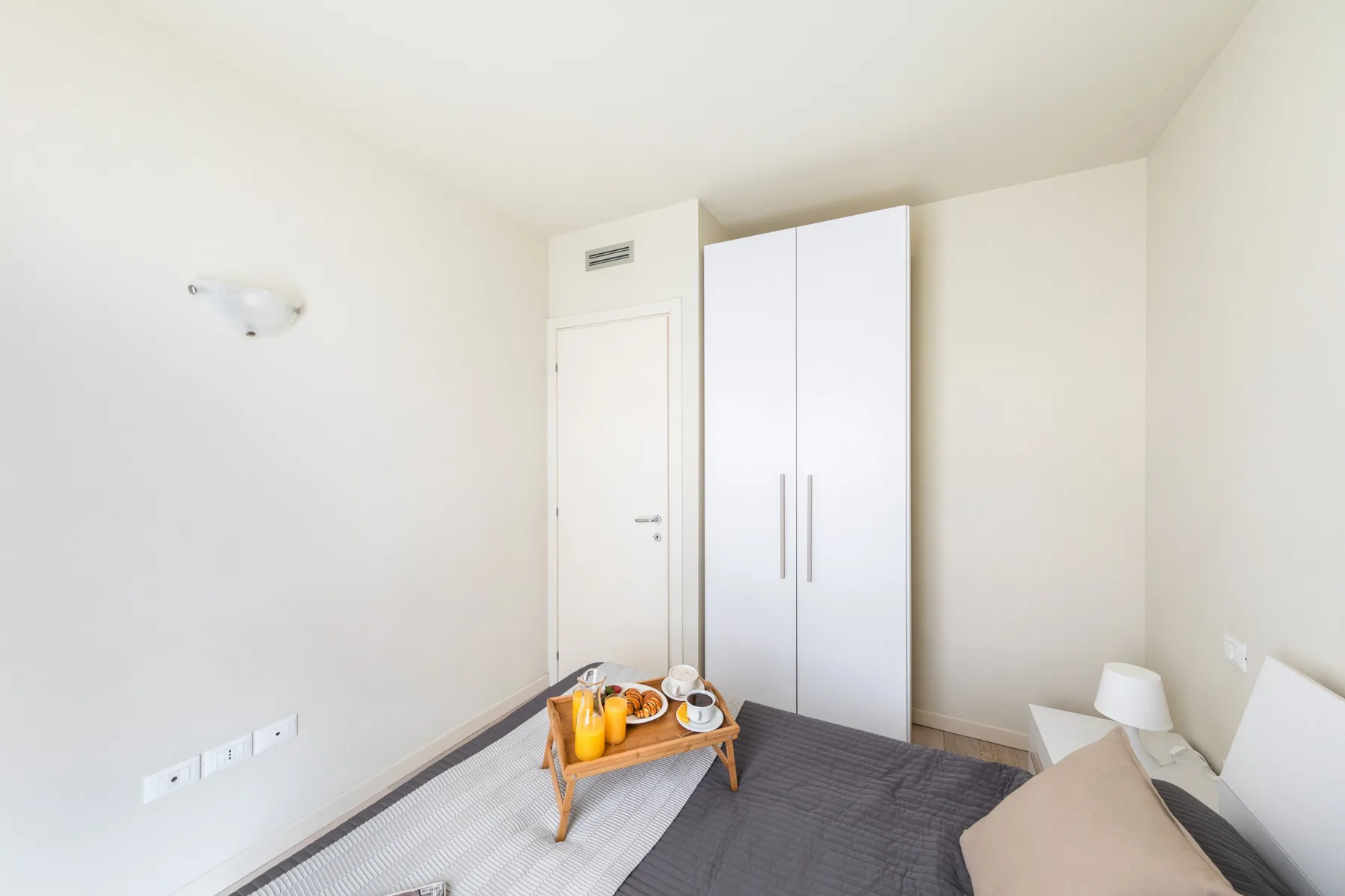 A bright bedroom with a bed, wardrobe, and small table.