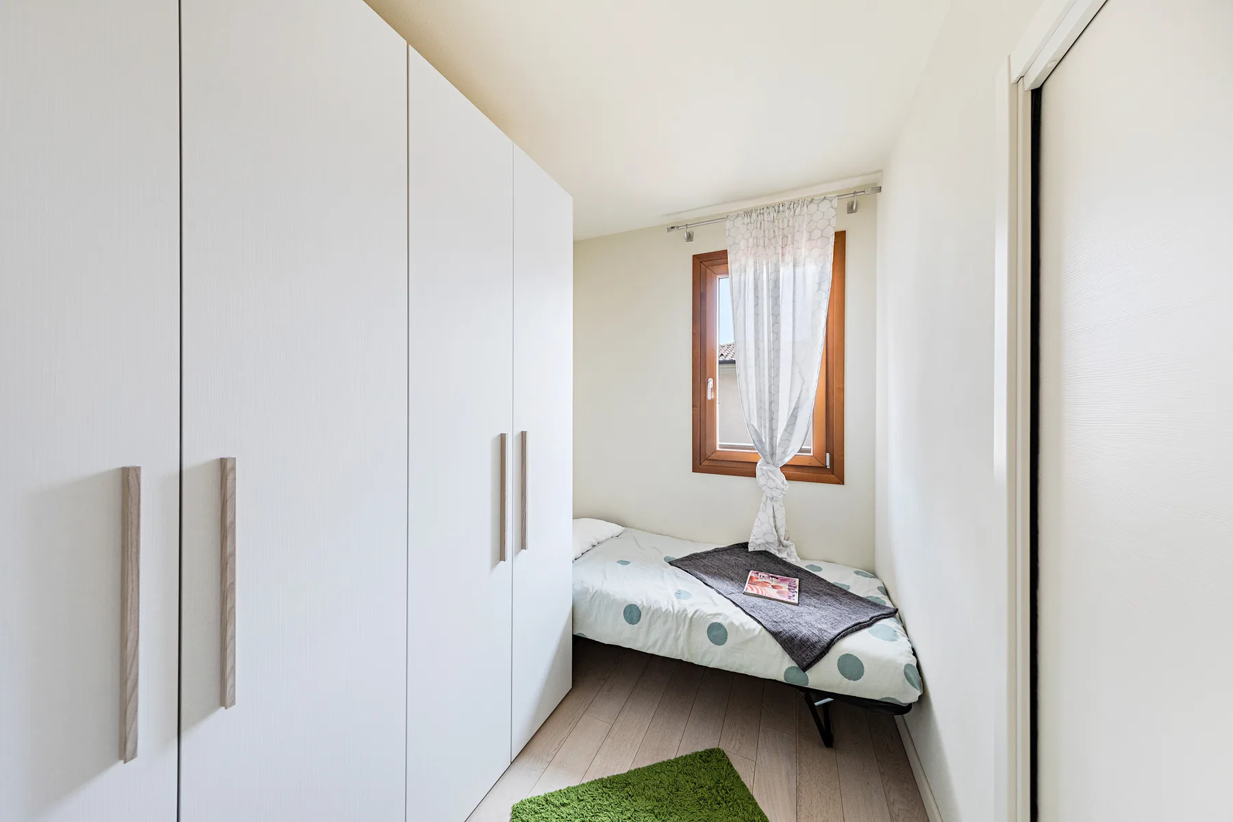 A narrow bedroom with a bed beside a large white wardrobe.