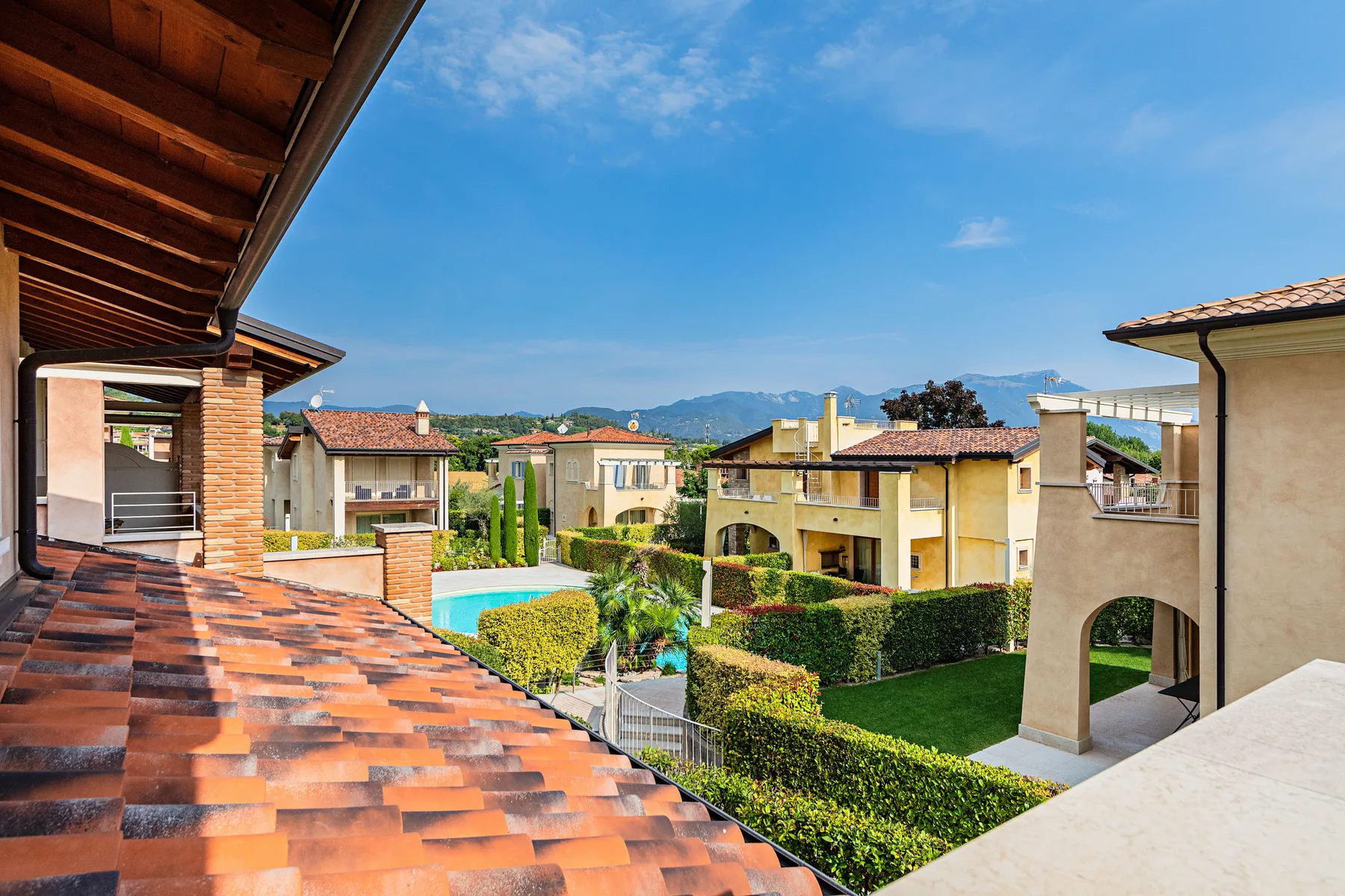 A rooftop terrace overlooks landscaped homes, a swimming pool, and distant mountains.