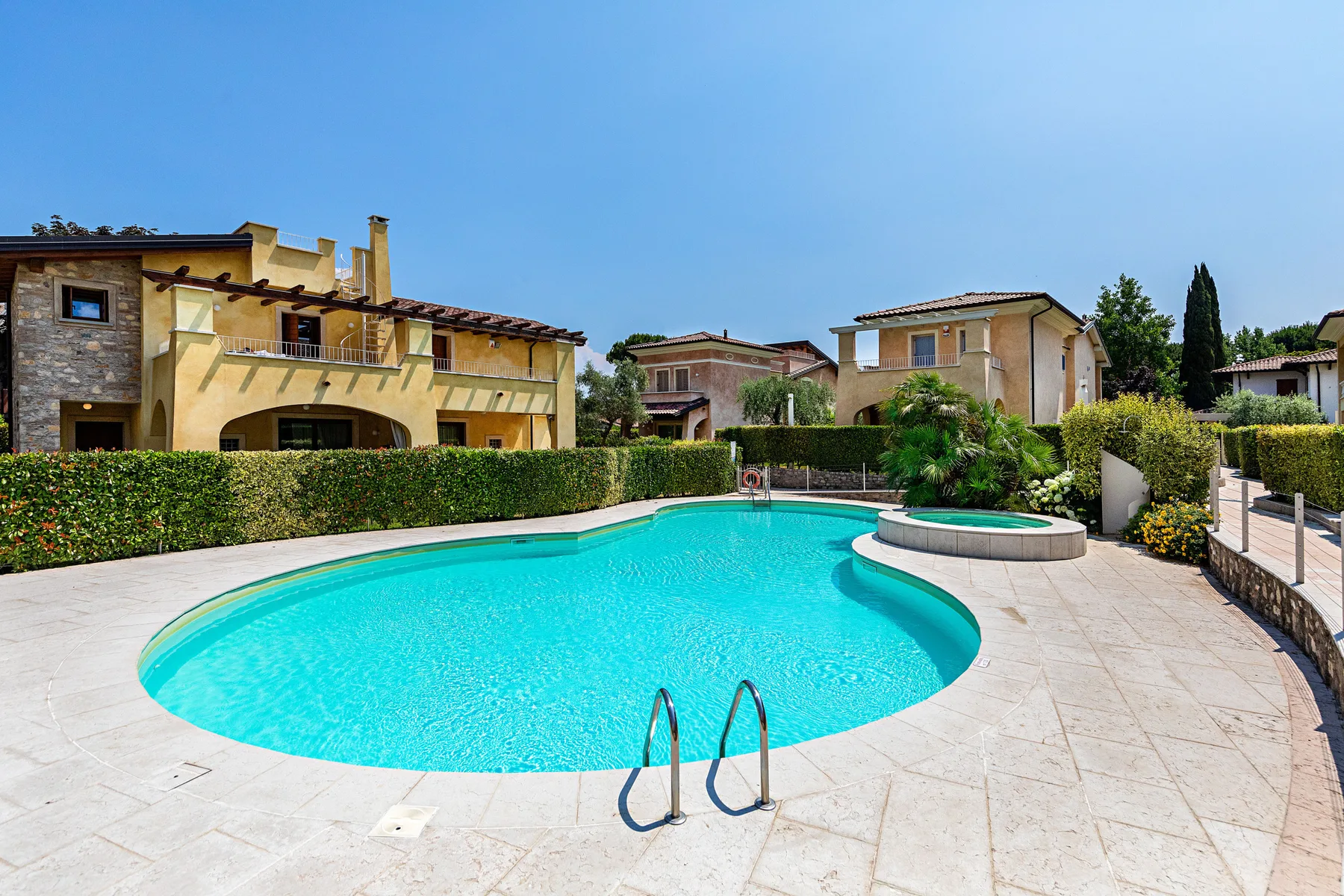 An outdoor swimming pool sits beside a paved patio and landscaped hedges.