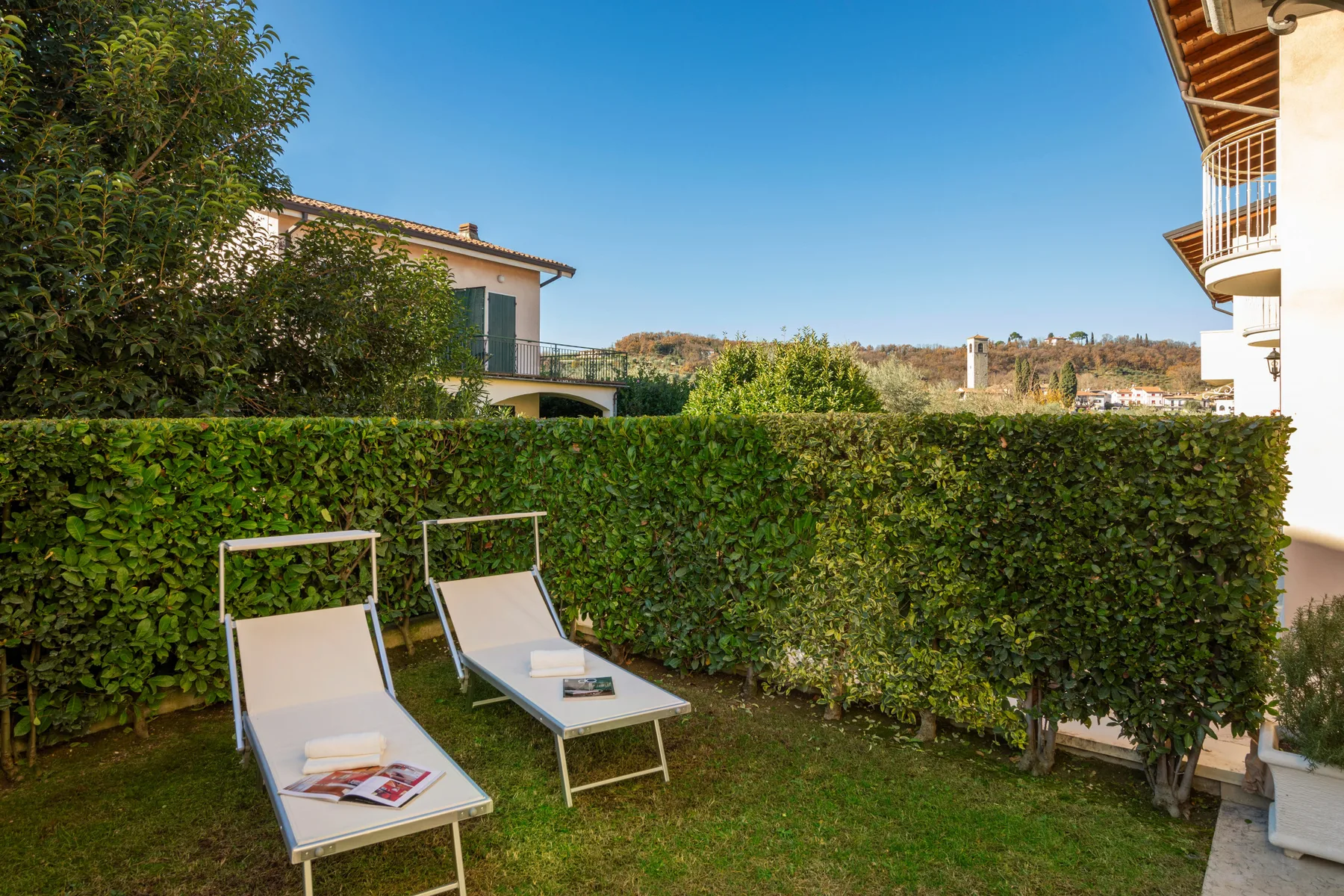 A garden seating area with two loungers facing a tall green hedge.