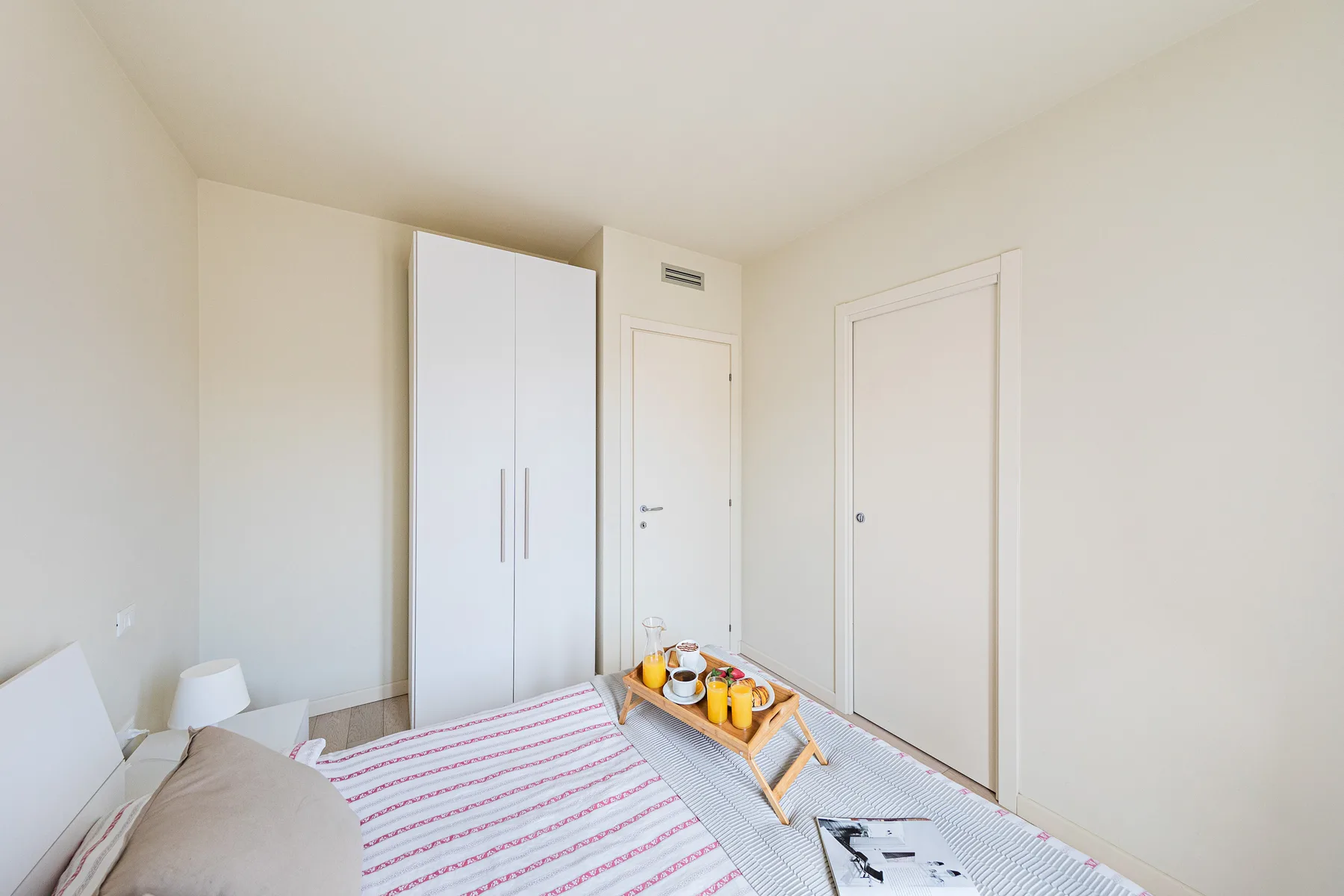 A bedroom with a bed and a small tray of drinks near the foot.