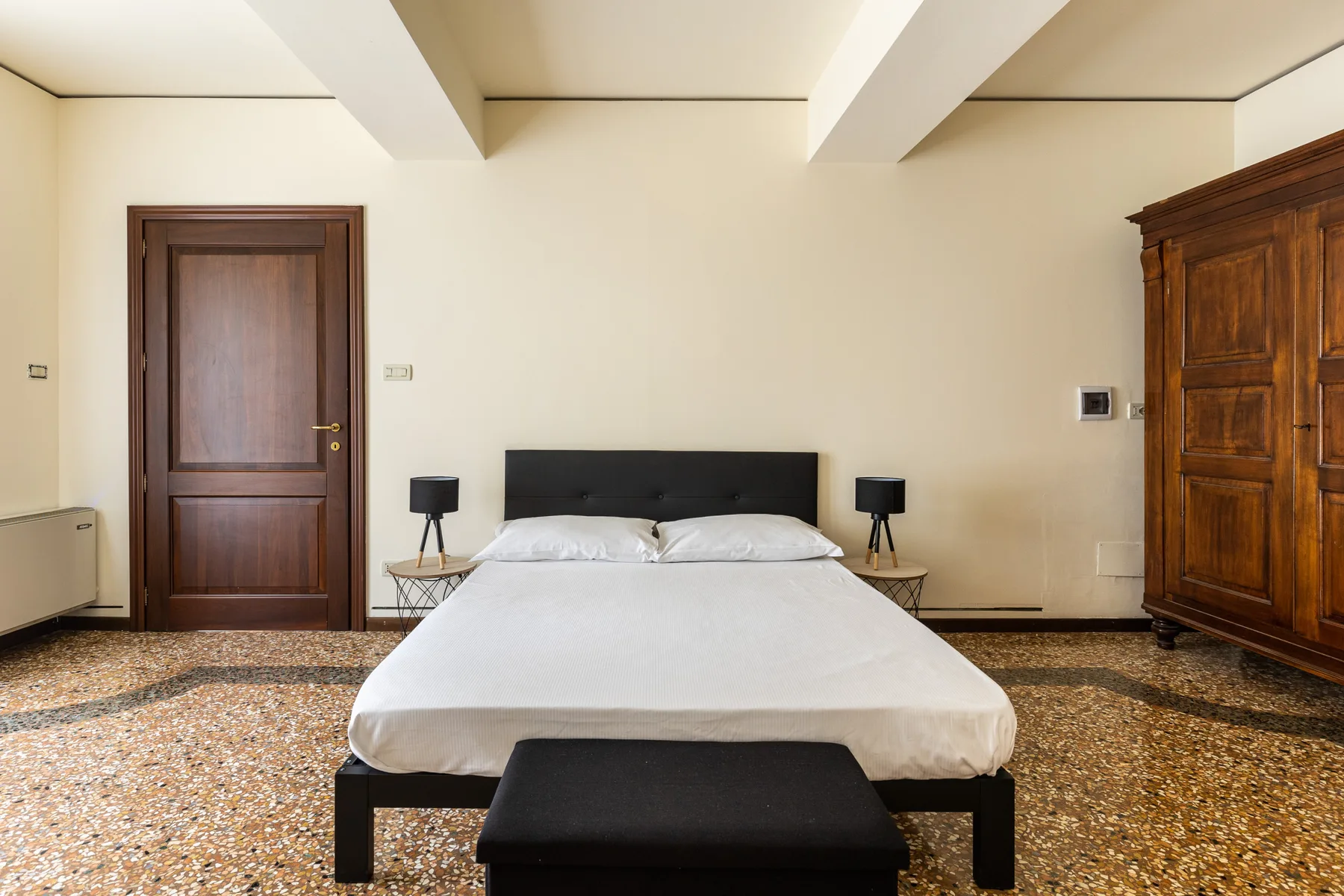 A bedroom with a double bed, bedside tables, and a large wooden wardrobe.
