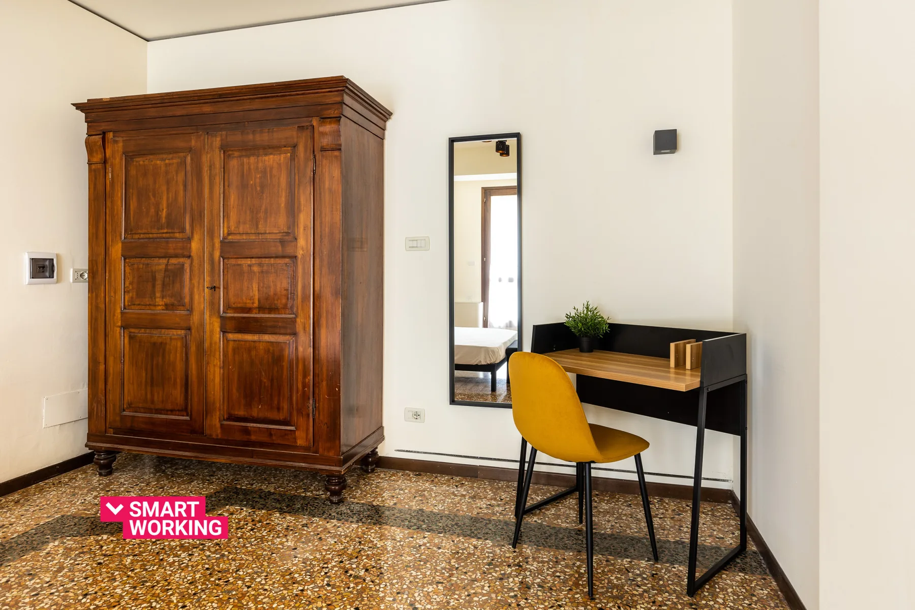 A bedroom workspace with a wooden wardrobe, desk, and yellow chair.