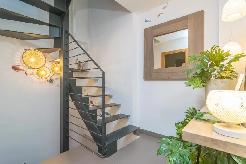 A bright interior with a dark metal staircase, wall mirror, and leafy plants.
