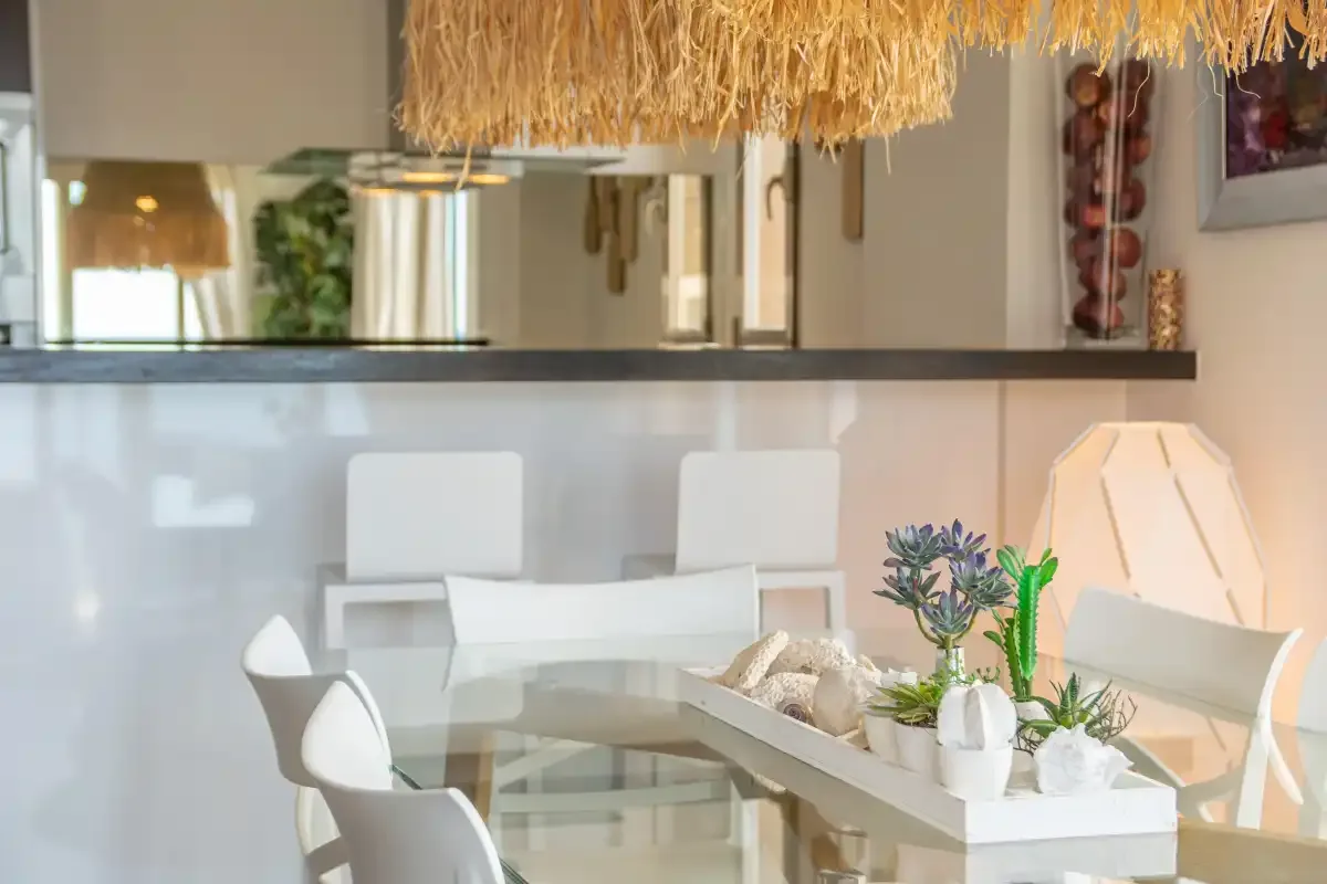 A bright dining area with a glass table, white seating, and a pendant lamp.