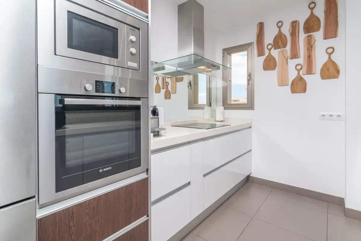 A modern kitchen with white cabinets, built-in appliances, and wooden cutting boards on the wall.