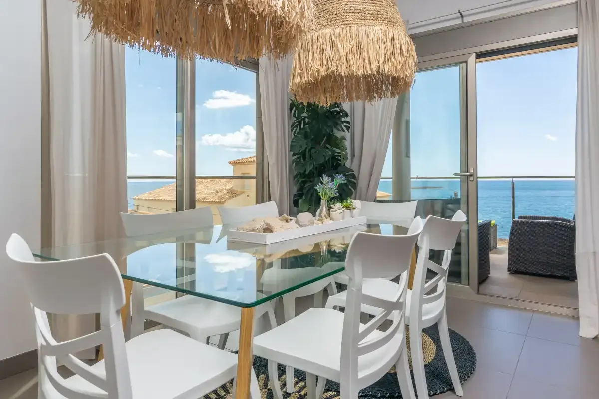 A bright dining area with a glass table and views of the sea.