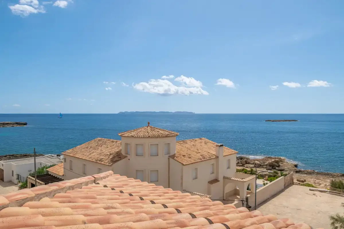 A coastal residence with terracotta roofs overlooks the blue sea beneath a clear sky.