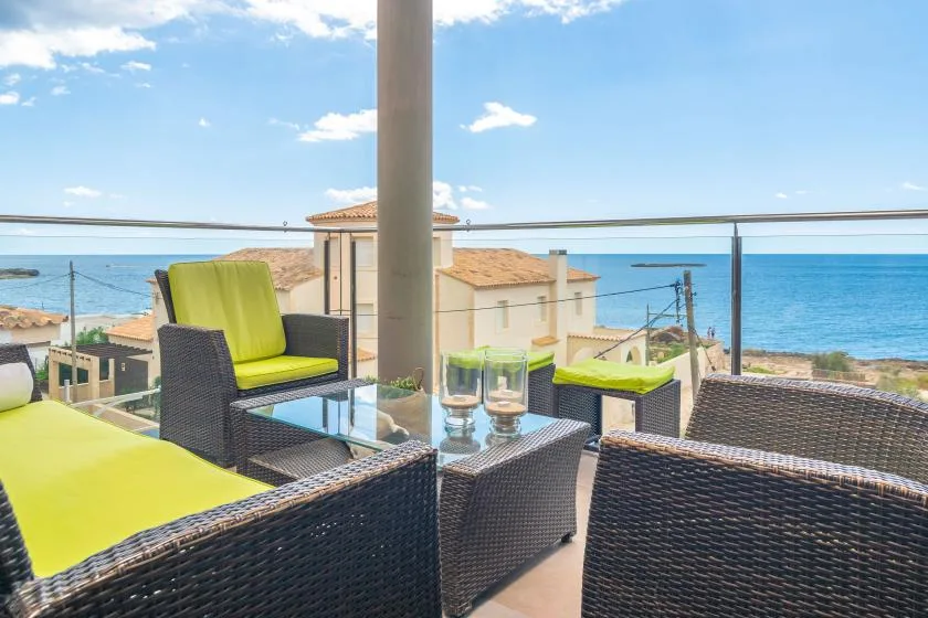 A sea-view terrace has dark woven seating with bright green cushions.