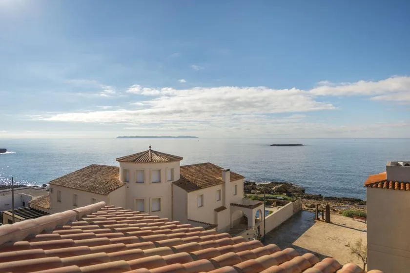 A coastal building with tiled roofs overlooks the sea beneath a partly cloudy sky.
