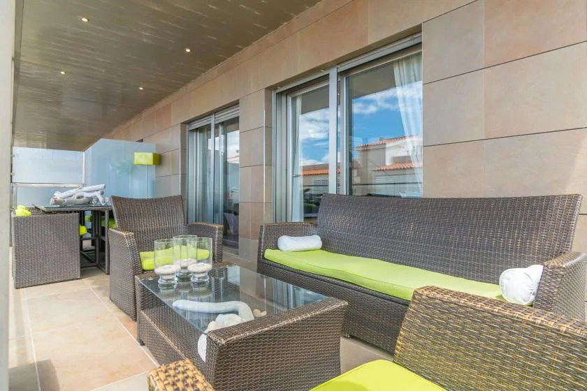 A covered outdoor seating area with woven furniture and glass doors.