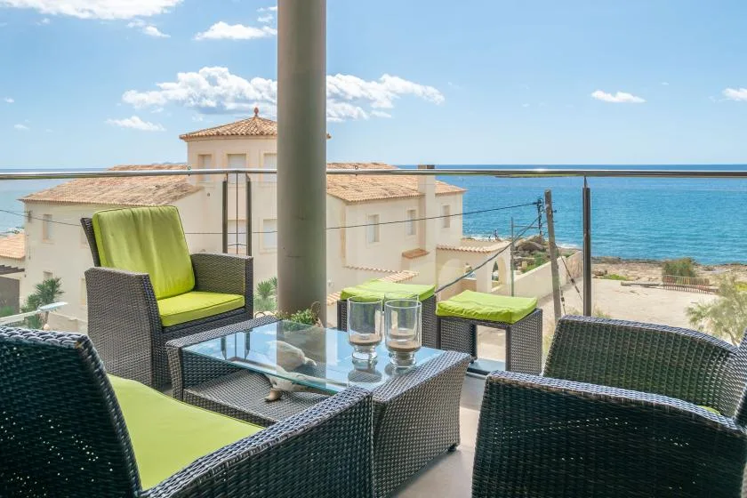 A balcony seating area with a glass table overlooks the sea.