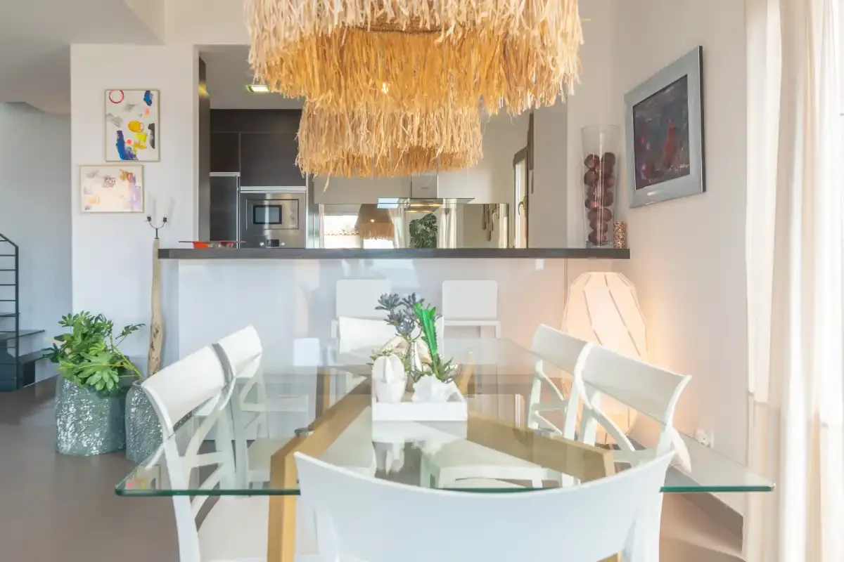 A dining area with a glass table and woven pendant light.