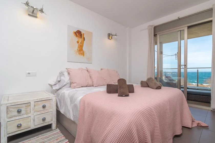 A bedroom with pink bedding and sliding glass doors overlooking the sea.