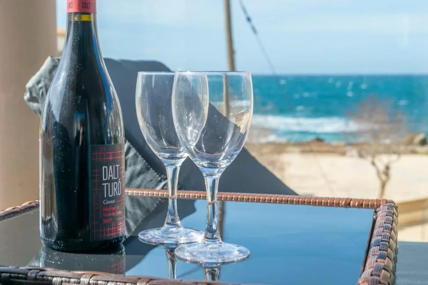 A bottle and wine glasses sit on a table overlooking the beach and sea.