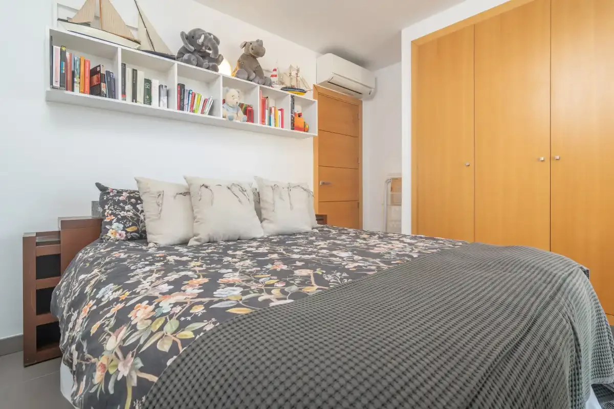 A bedroom with a bed beneath a wall-mounted bookshelf.