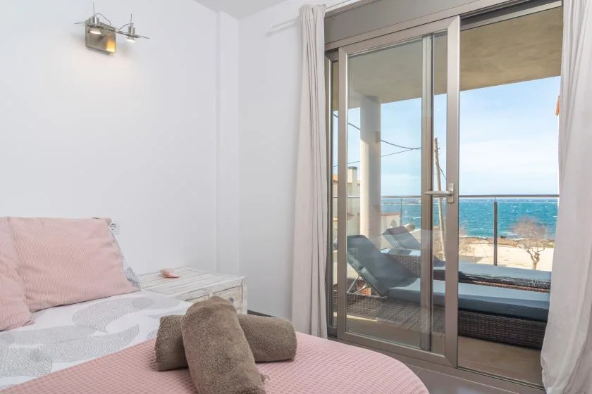 A bedroom opens onto a balcony with seating and a view of the sea.