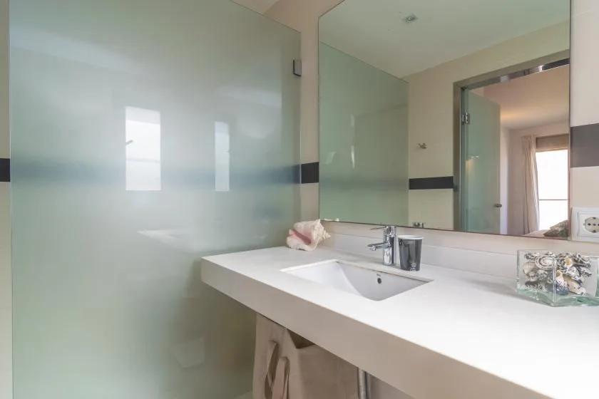 A bathroom vanity with a wide white counter, sink, and large mirror.