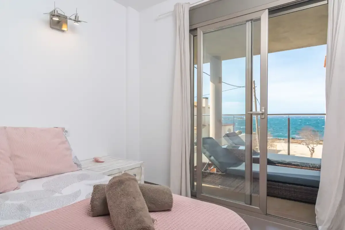 A bedroom opens onto a balcony with seating and a view of the sea.
