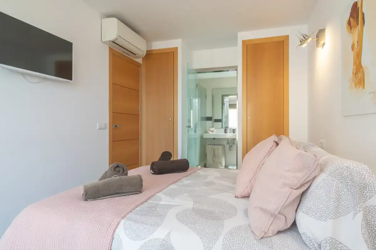 A bedroom with a neatly made bed and an open doorway to the bathroom.
