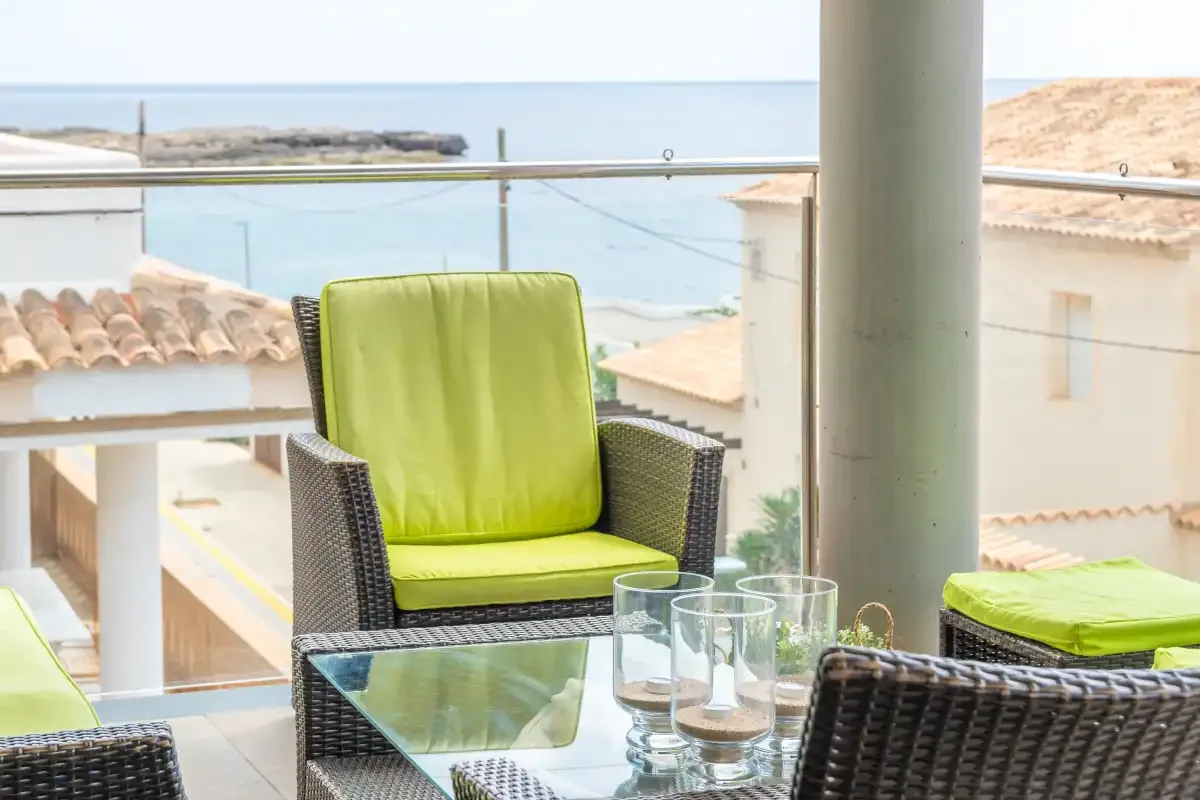 A balcony seating area with a glass table overlooks the sea.