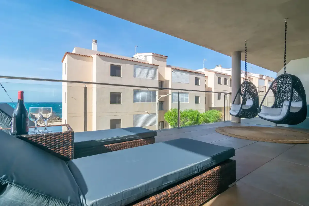A covered balcony with cushioned seating and hanging chairs overlooks the sea.