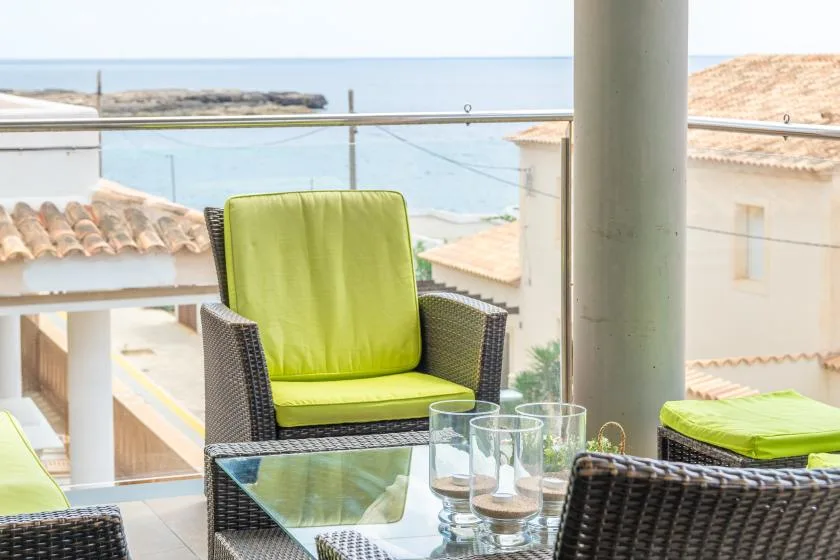 A balcony seating area overlooks the water, with bright green cushions and glassware.