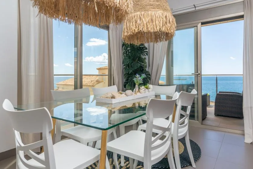 A dining area with a glass table and large windows overlooking the sea.