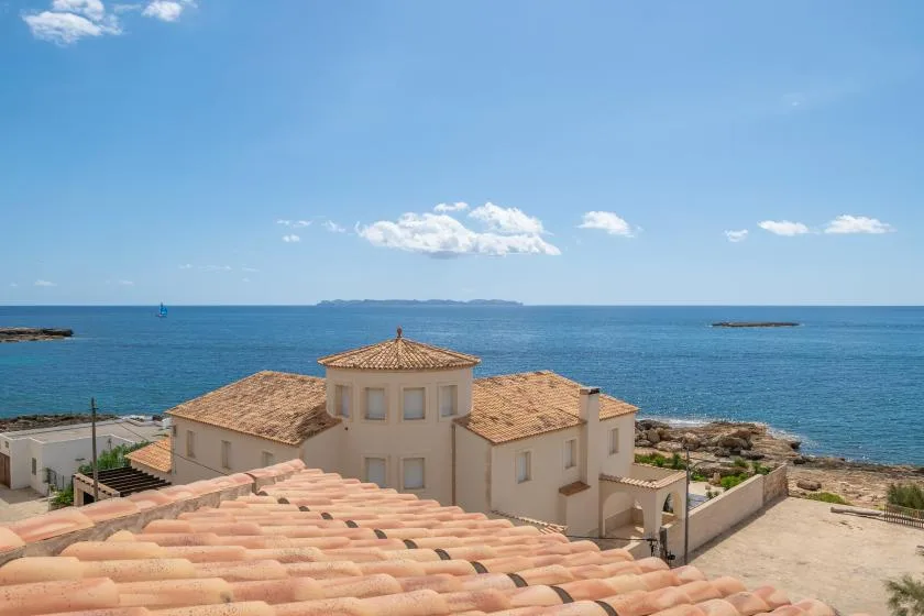 Coastal buildings with terracotta roofs overlook the sea beneath a blue sky.