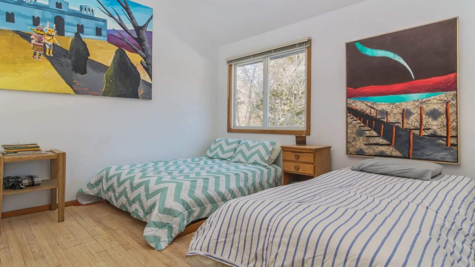 A bedroom with two beds, framed artwork, and a window.